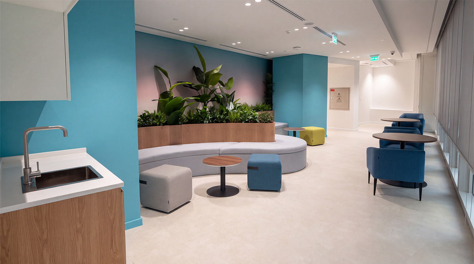 Blue-toned lounge with curved shared seating, tables and plants.